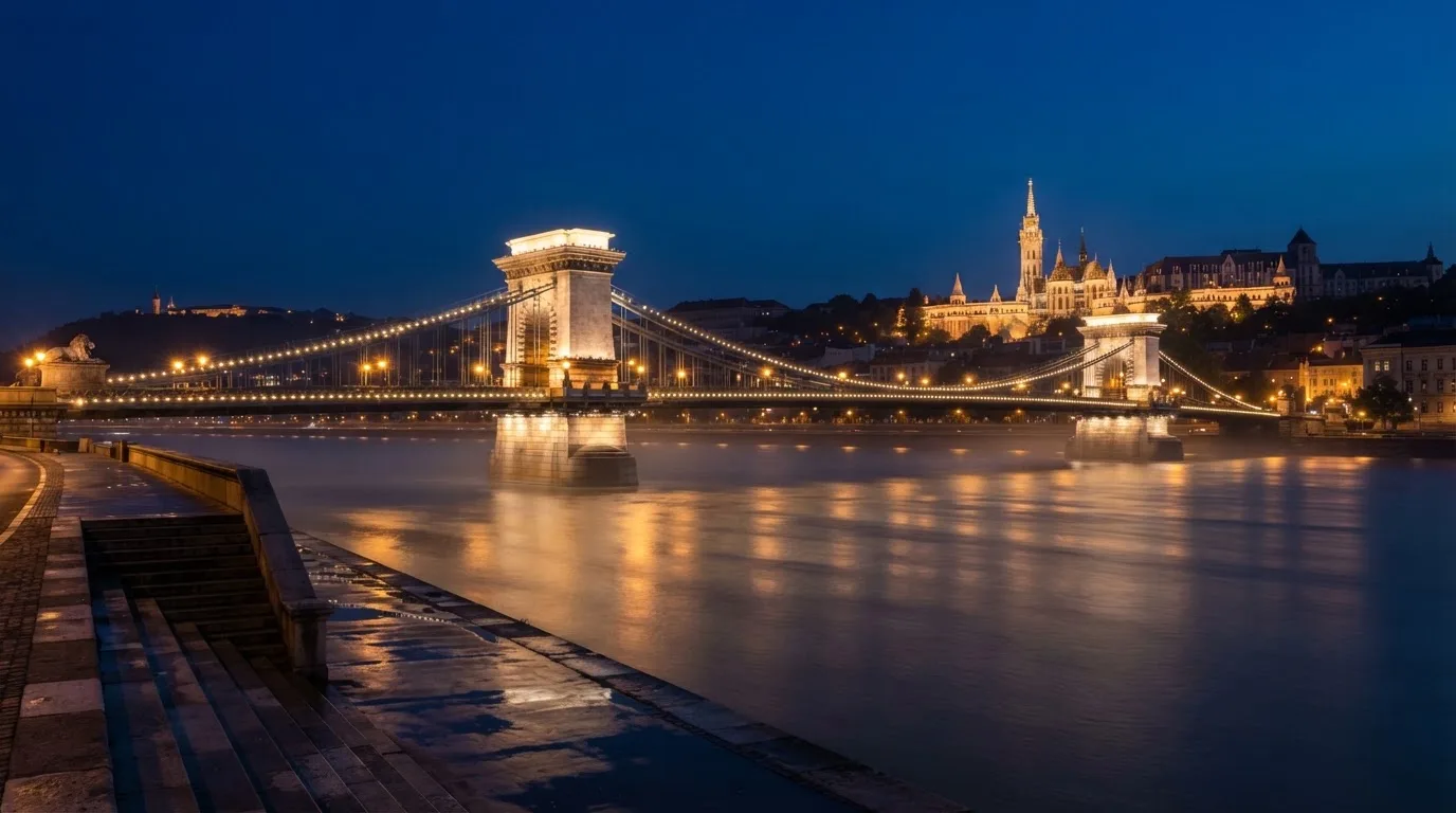A budapesti Lánchíd esti fényekben a Duna fölött, a háttérben a budai Vár, forgalom nélküli rakpart.
